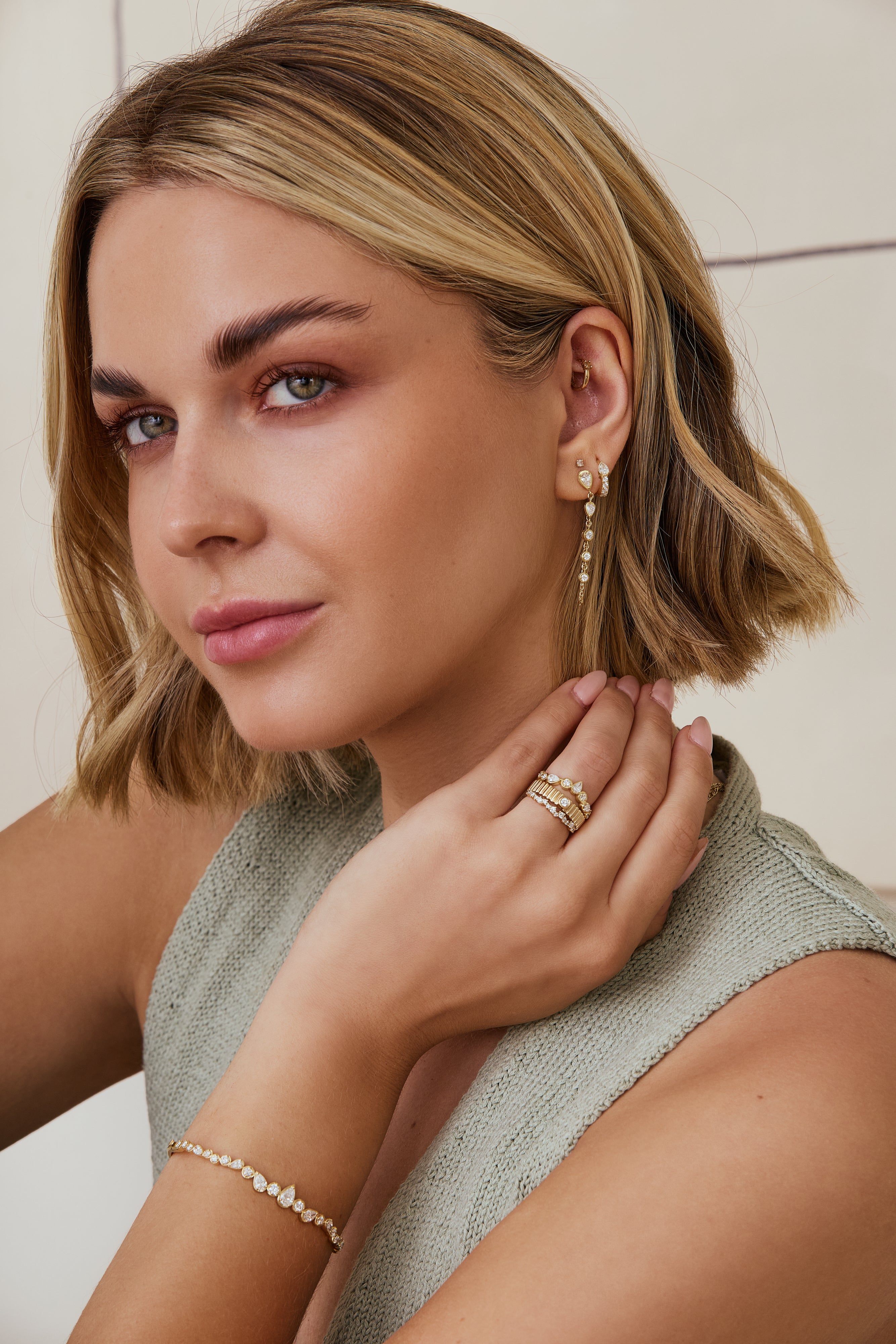 Woman wearing gold earrings, ring, and bracelet against a neutral background