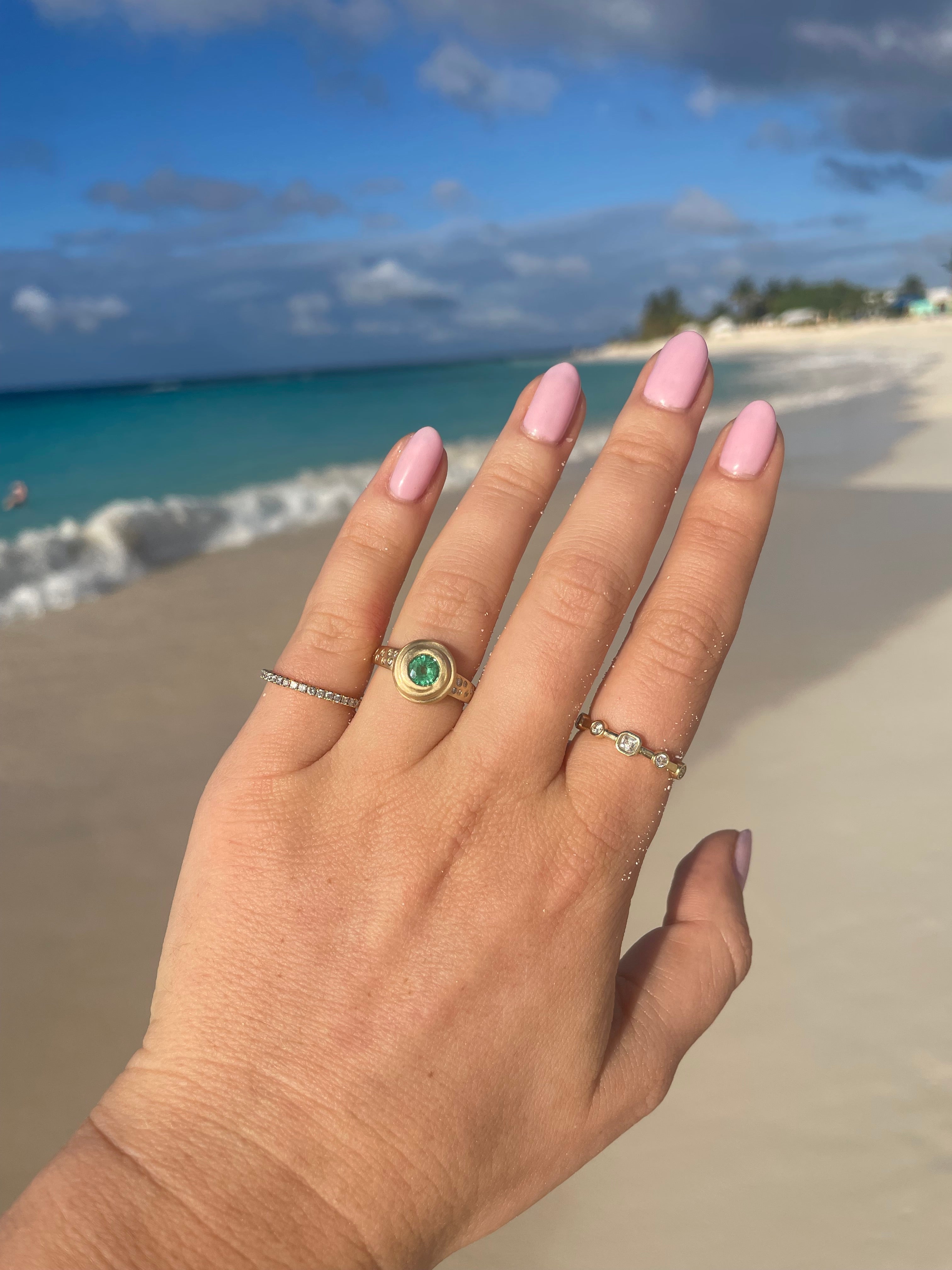 woman's hand at beach with gold, emerald and diamond rings by carter eve jewelry