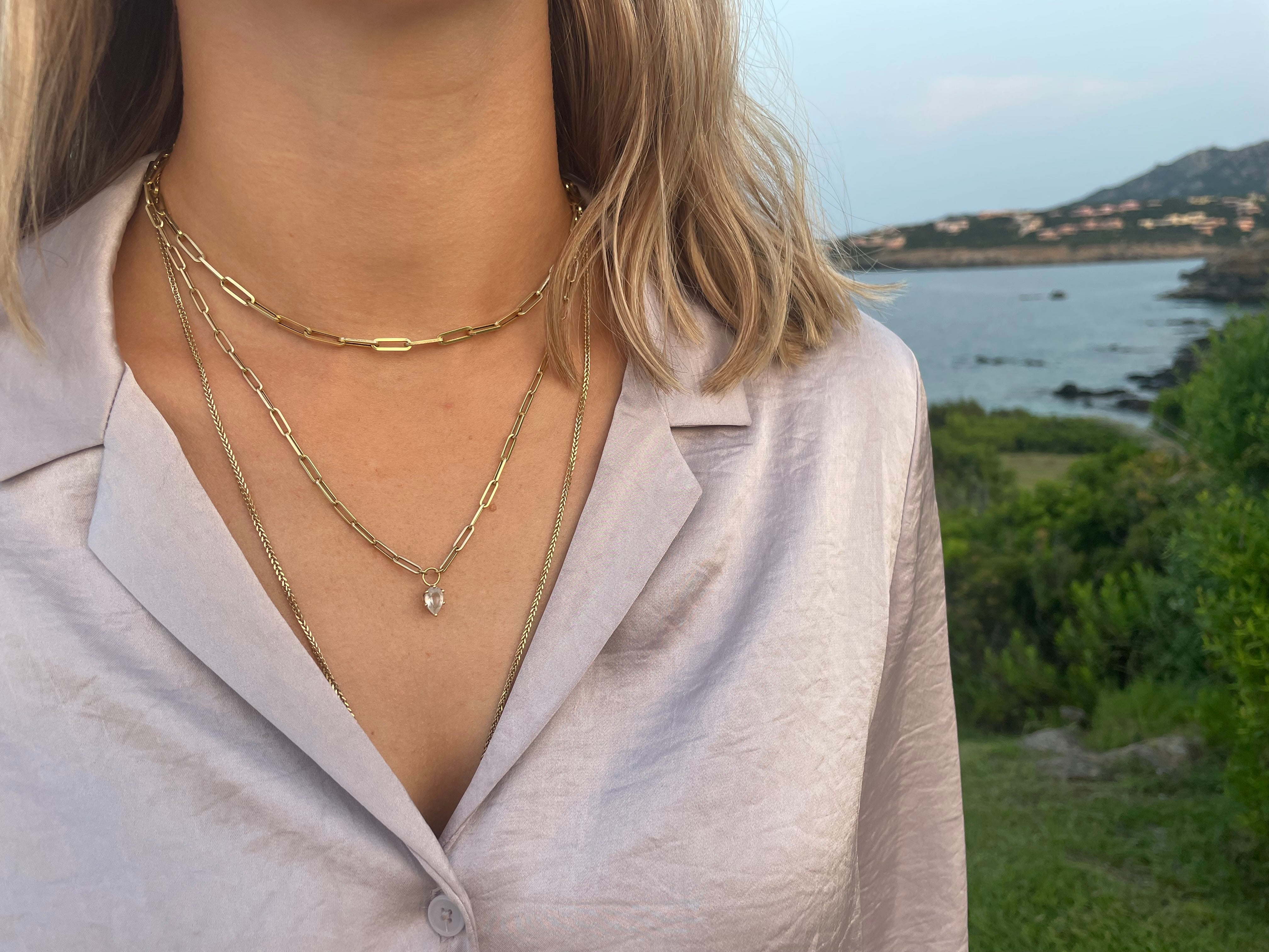 Person wearing a gold necklace with a scenic background of water and greenery