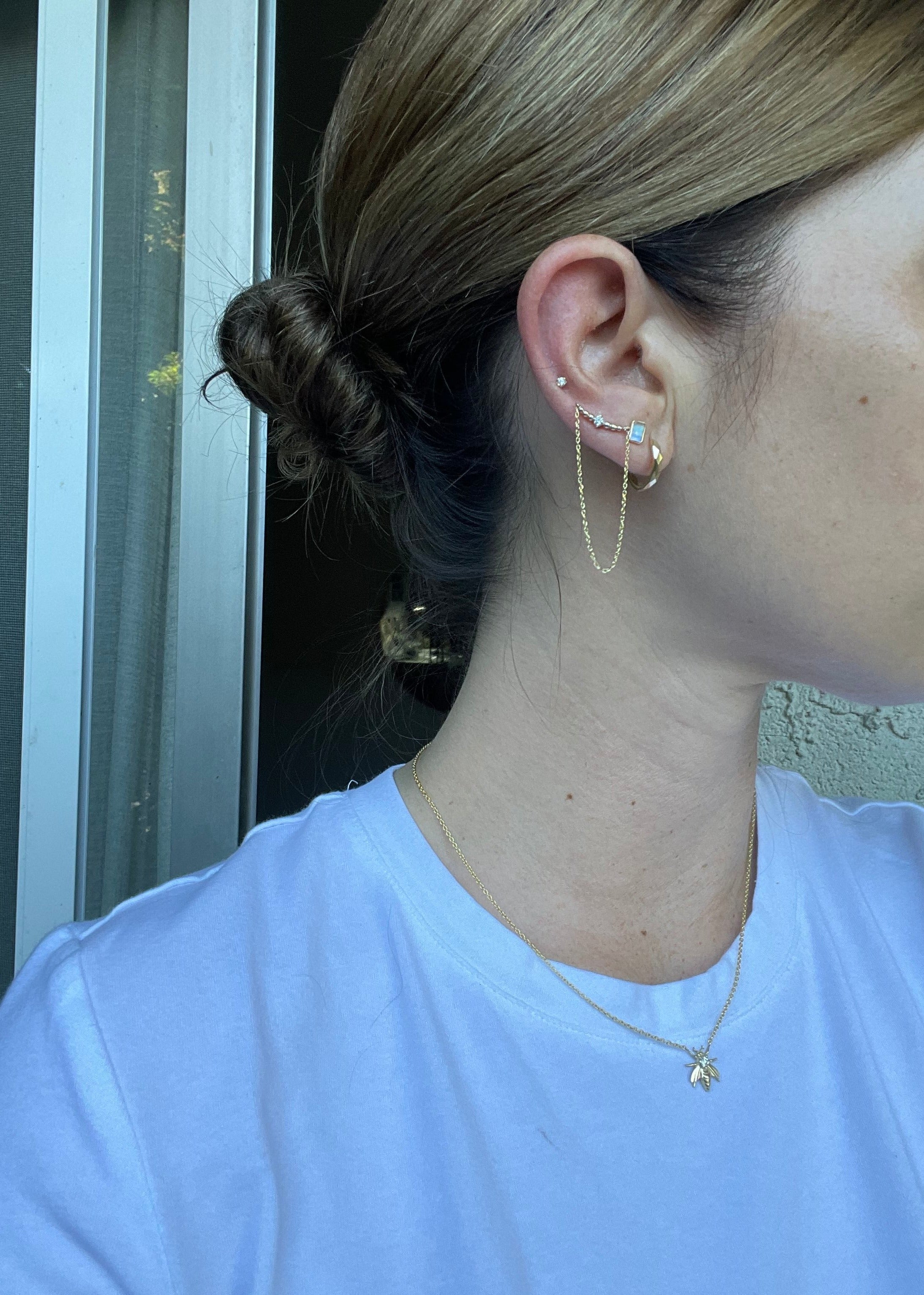 woman wearing a hoop earring, stud earring and double chain drop earring and gold bee necklace