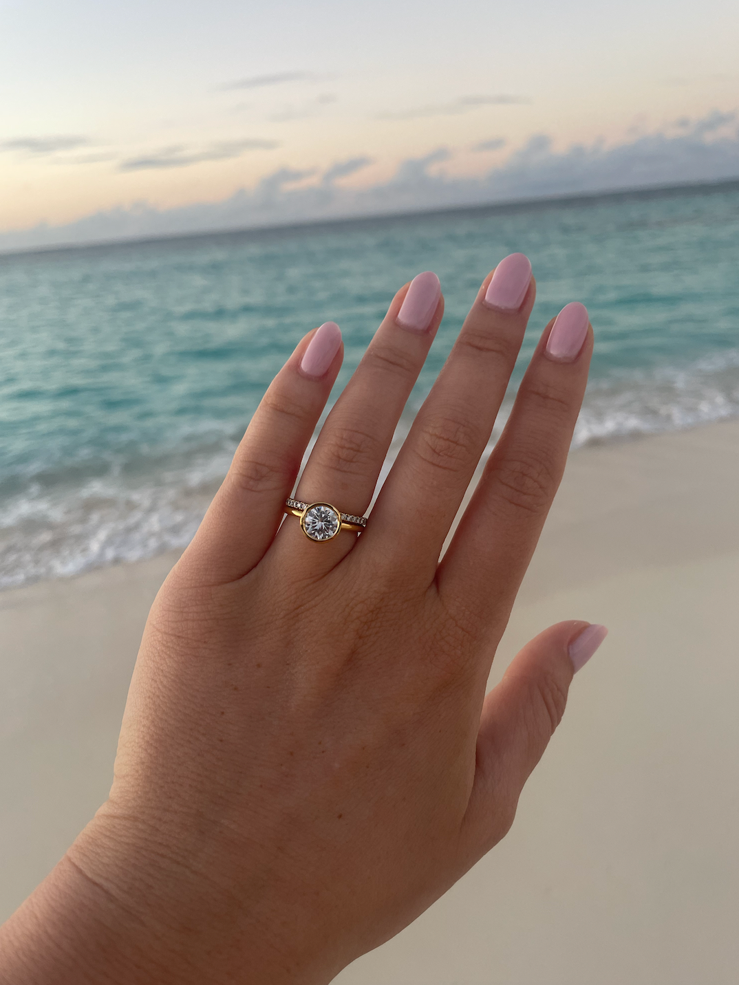 woman wearing round diamond engagement ring with diamond eternity wedding band on the beach