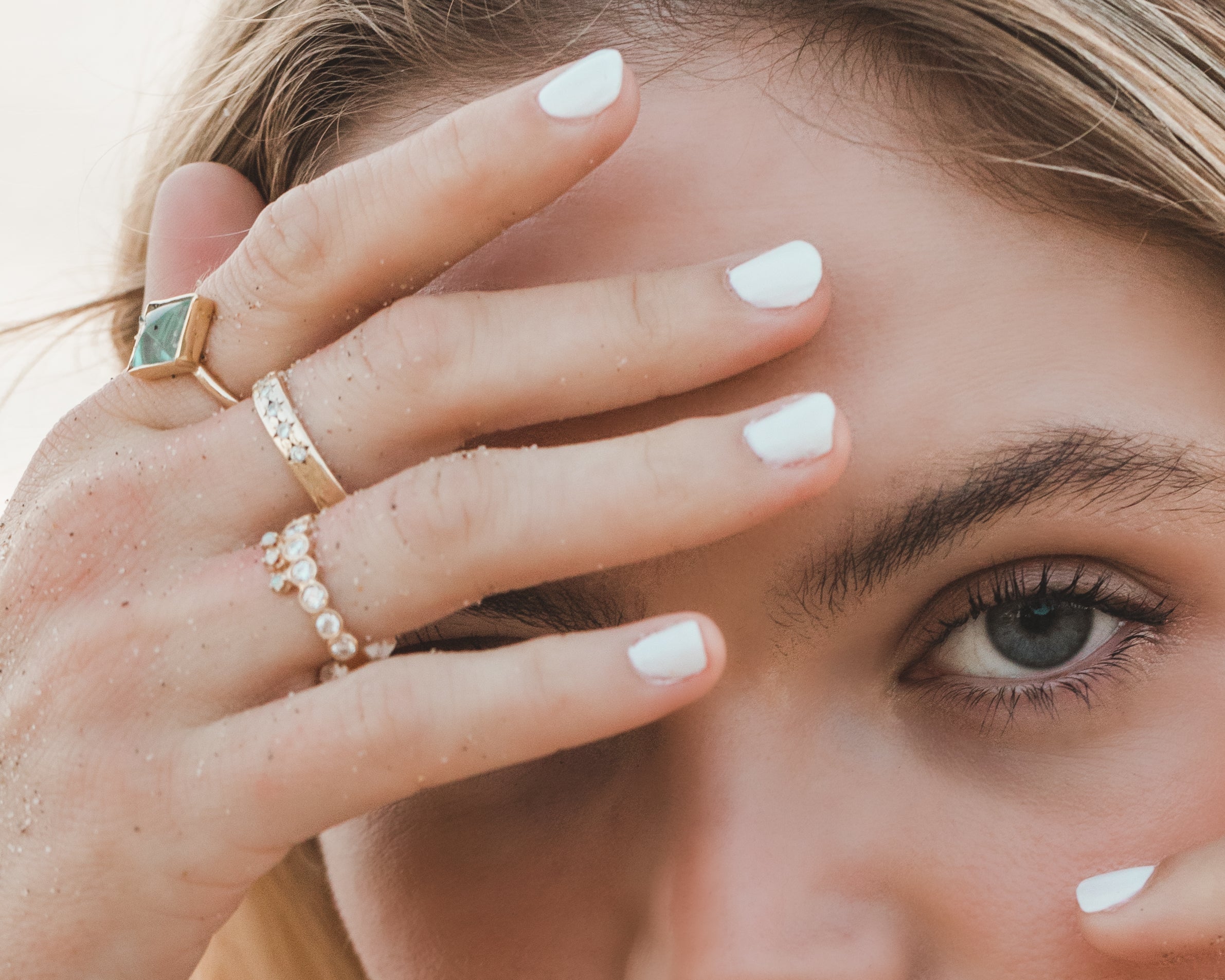 Woman wearing three gold, diamond and aquamarine rings. Shop with Carter Eve Jewelry for a touch of luxury.