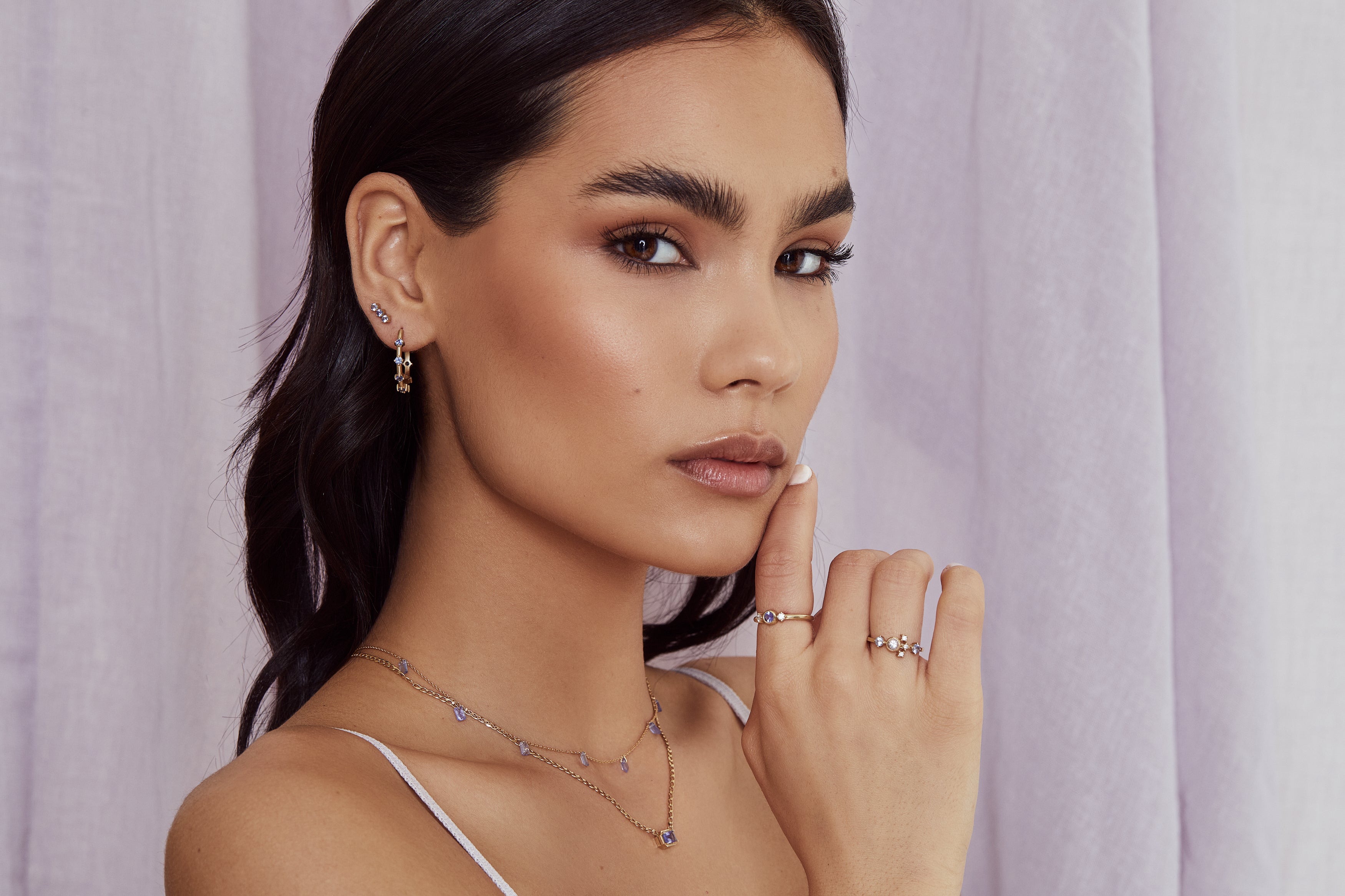 elegant woman wearing 14ky gold and sapphire earrings, 14ky gold and tanzanite necklaces and two gold rings with sapphires and diamonds. Shop now for a touch of luxury.